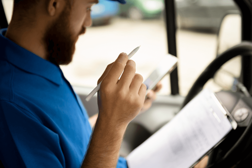 Caminhoneiro de camisa azul, sentado no banco de motorista analisando papelada de DOT e Drug & Alcohol Compliance 