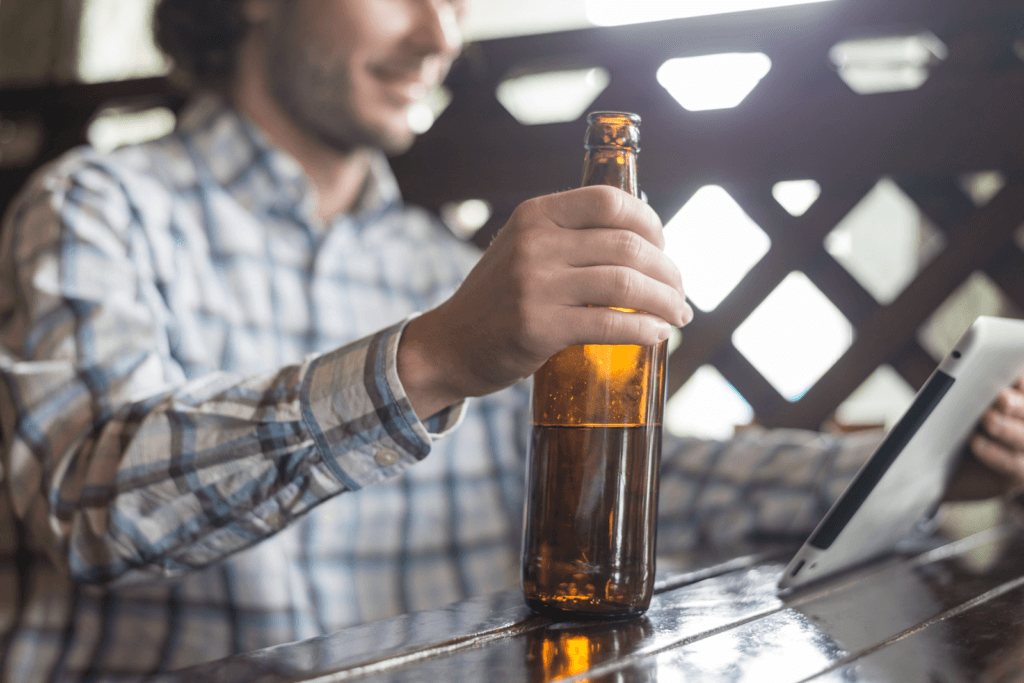 Truck driver standing at a table drinking a beer, going against Drug & Alcohol Compliance policies and putting his safety at risk